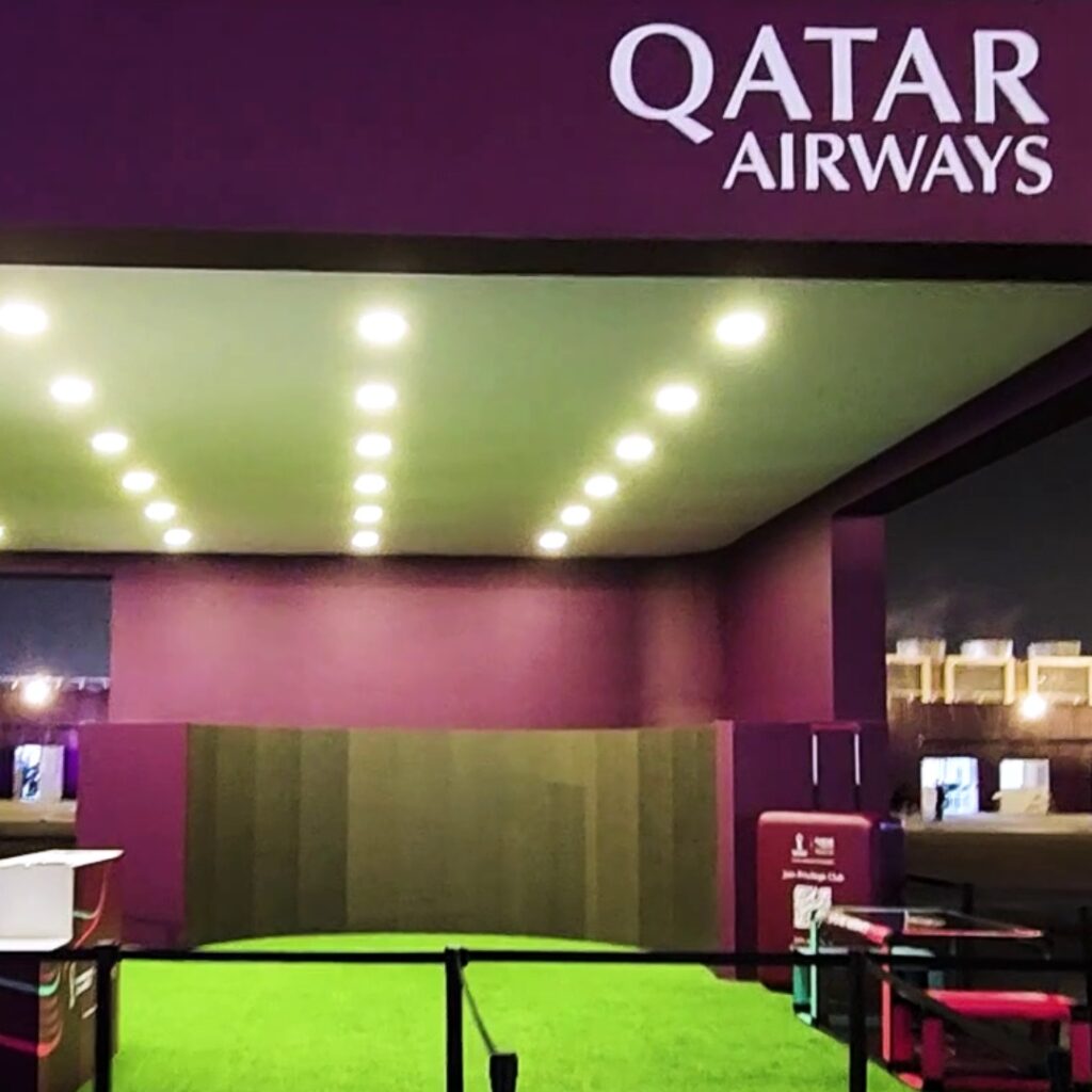 A Qatar Airways exhibition booth with a big curved screen. The setup includes bright overhead lights and green carpeting.