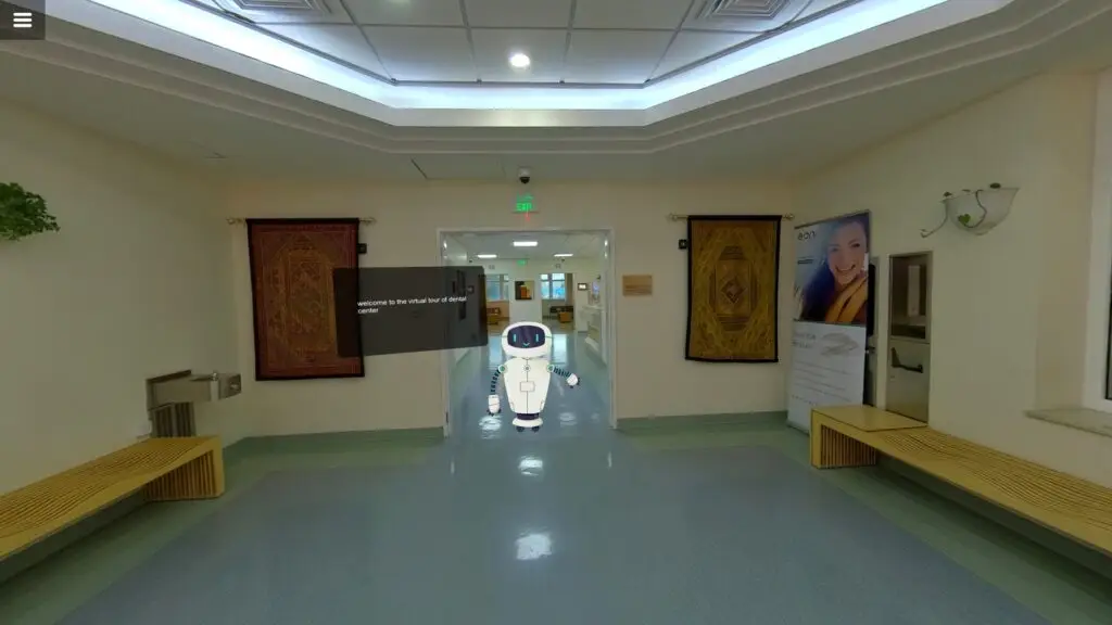 A preview of a virtual experience of a hospital showing a hallway with soft lighting and light walls. In the center, a small, white robot stands on a glossy floor.