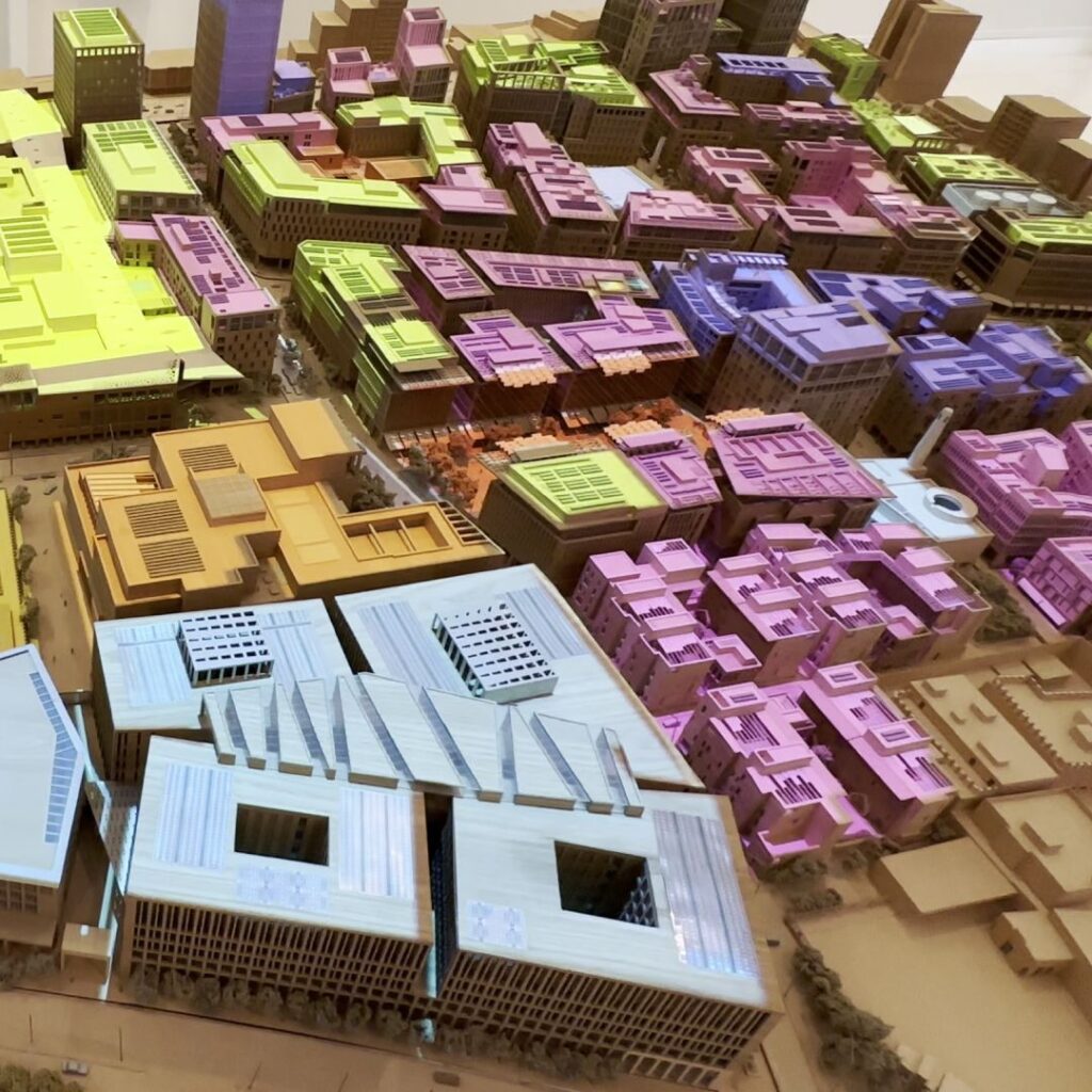 A wooden architectural model of a city, featuring buildings colored by projection from ceiling, indicating different zones or purposes. The model includes streets, mosques, and distinct architectural designs.