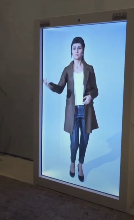 A digital display showcases a female virtual avatar standing in a holobox. Set against a light blue background, the avatar gestures with one hand, demonstrating inaion advanced AI solution, a product by Vraxa.