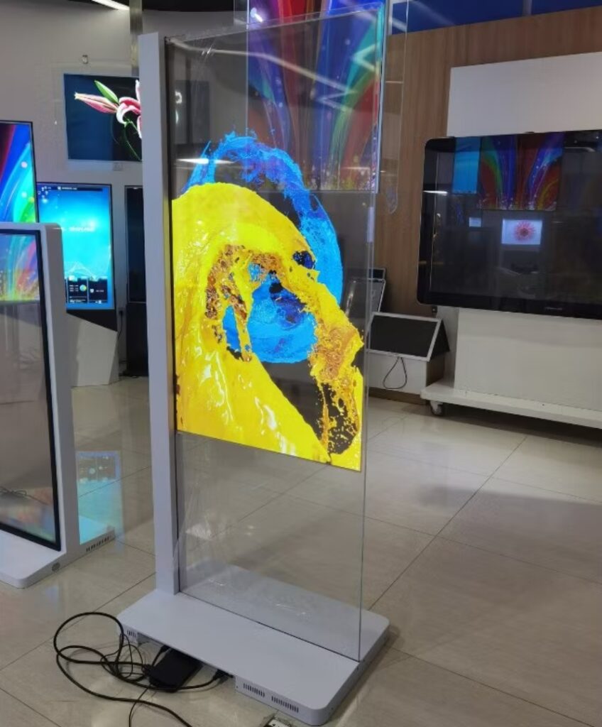 A transparent display screen on a stand showcases a vibrant abstract design with swirling blue and yellow colors, perfectly complementing the modern aesthetics of rooms. The scene is enhanced by other digital displays and light-colored flooring, creating a harmonious tech-savvy ambiance.