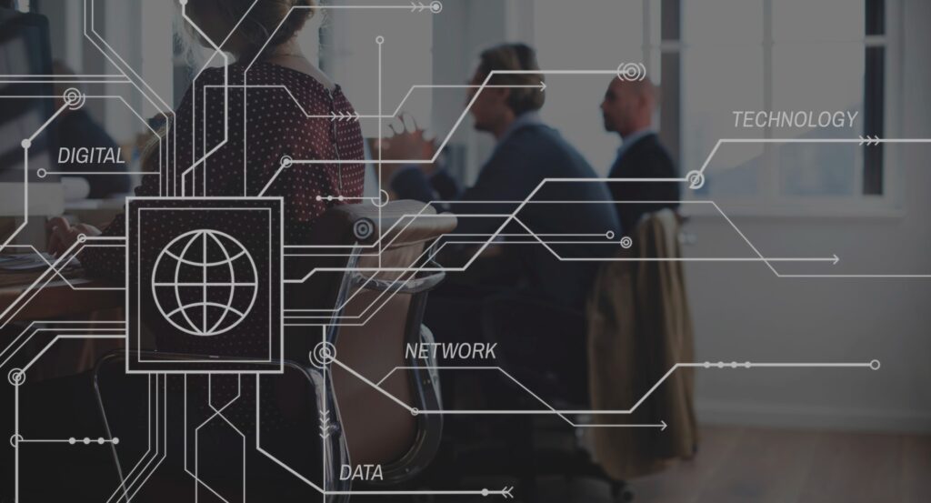 People are sitting at a table in a meeting room, blurred in the background. Overlay graphics include words like Digital, Network, Technology, and Data alongside Vraxa subsidiaries, with circuit-like lines and a globe icon on the left side.