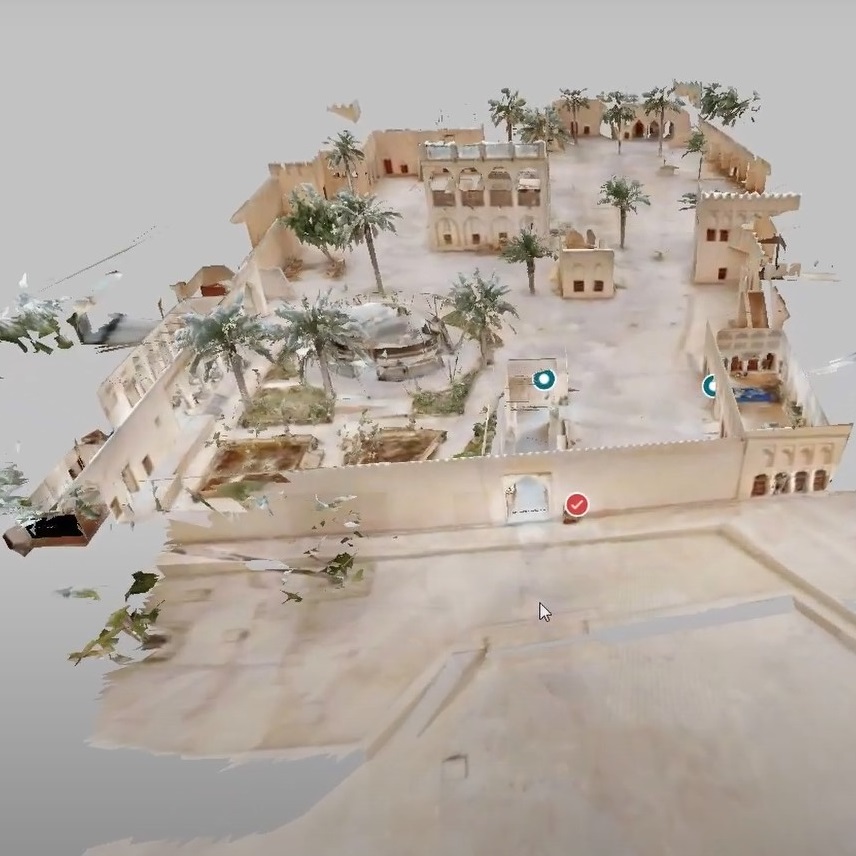 3D model of a historic desert fortress, featuring sandy-colored walls, courtyards, and scattered palm trees. There are several buildings within the enclosure, and some digital markers are visible. The scene is partially transparent.