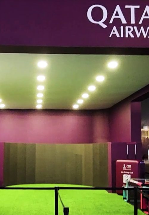 A Qatar Airways exhibition booth with a big curved screen. The setup includes bright overhead lights and green carpeting.