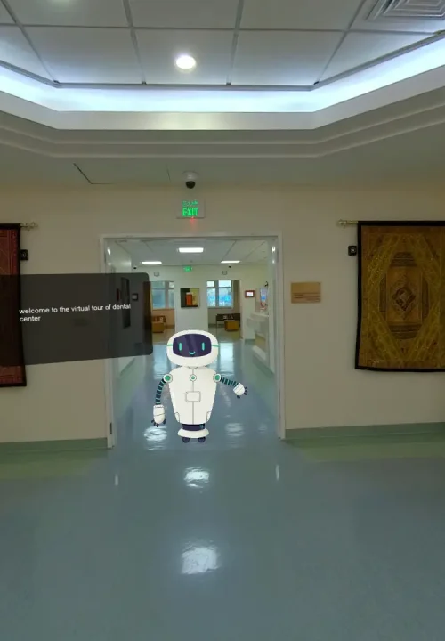 A preview of a virtual experience of a hospital showing a hallway with soft lighting and light walls. In the center, a small, white robot stands on a glossy floor.