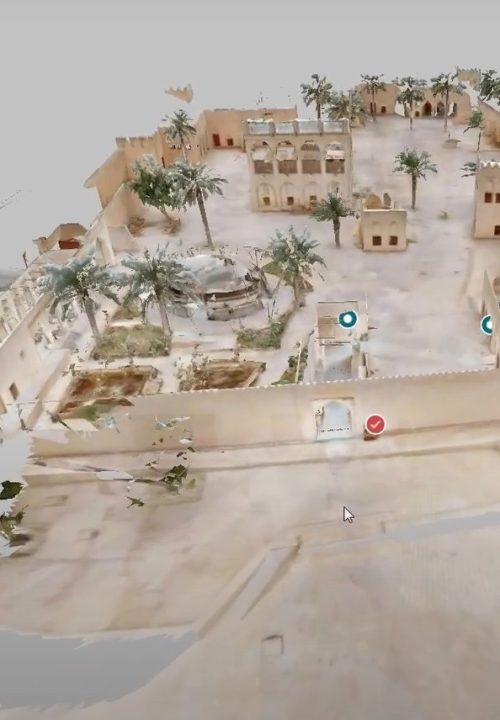 3D model of a historic desert fortress, featuring sandy-colored walls, courtyards, and scattered palm trees. There are several buildings within the enclosure, and some digital markers are visible. The scene is partially transparent.